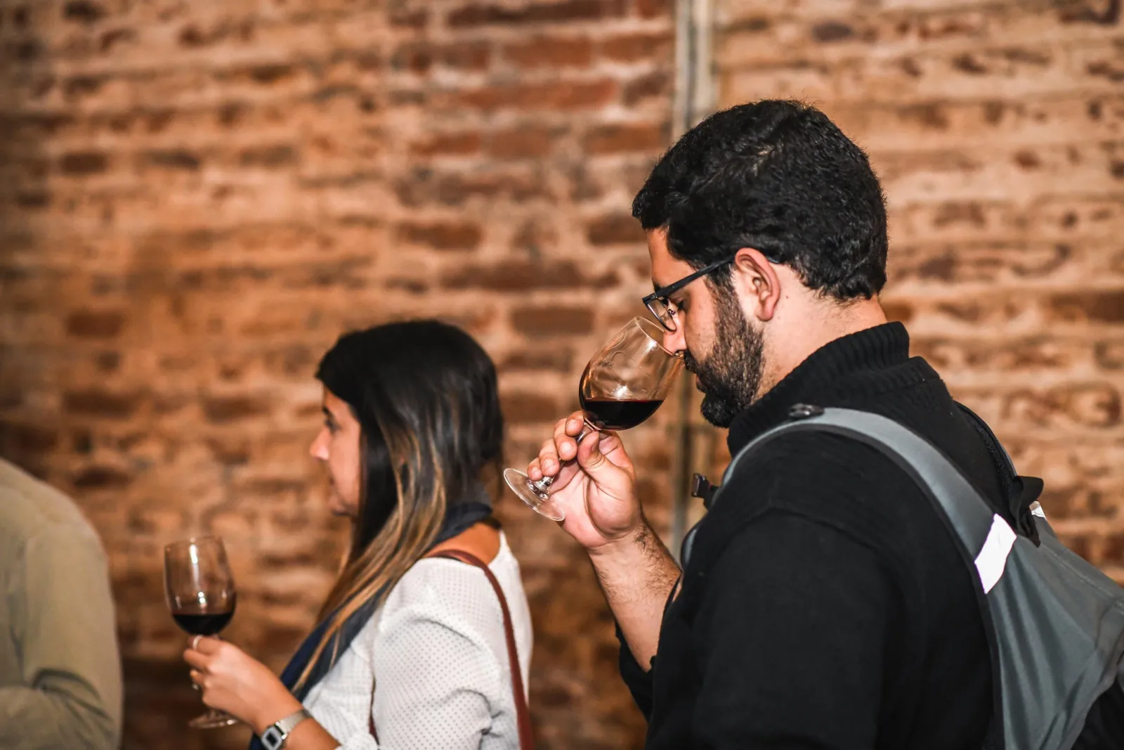 Visitor smelling a glass of red wine in front of an old brick wall