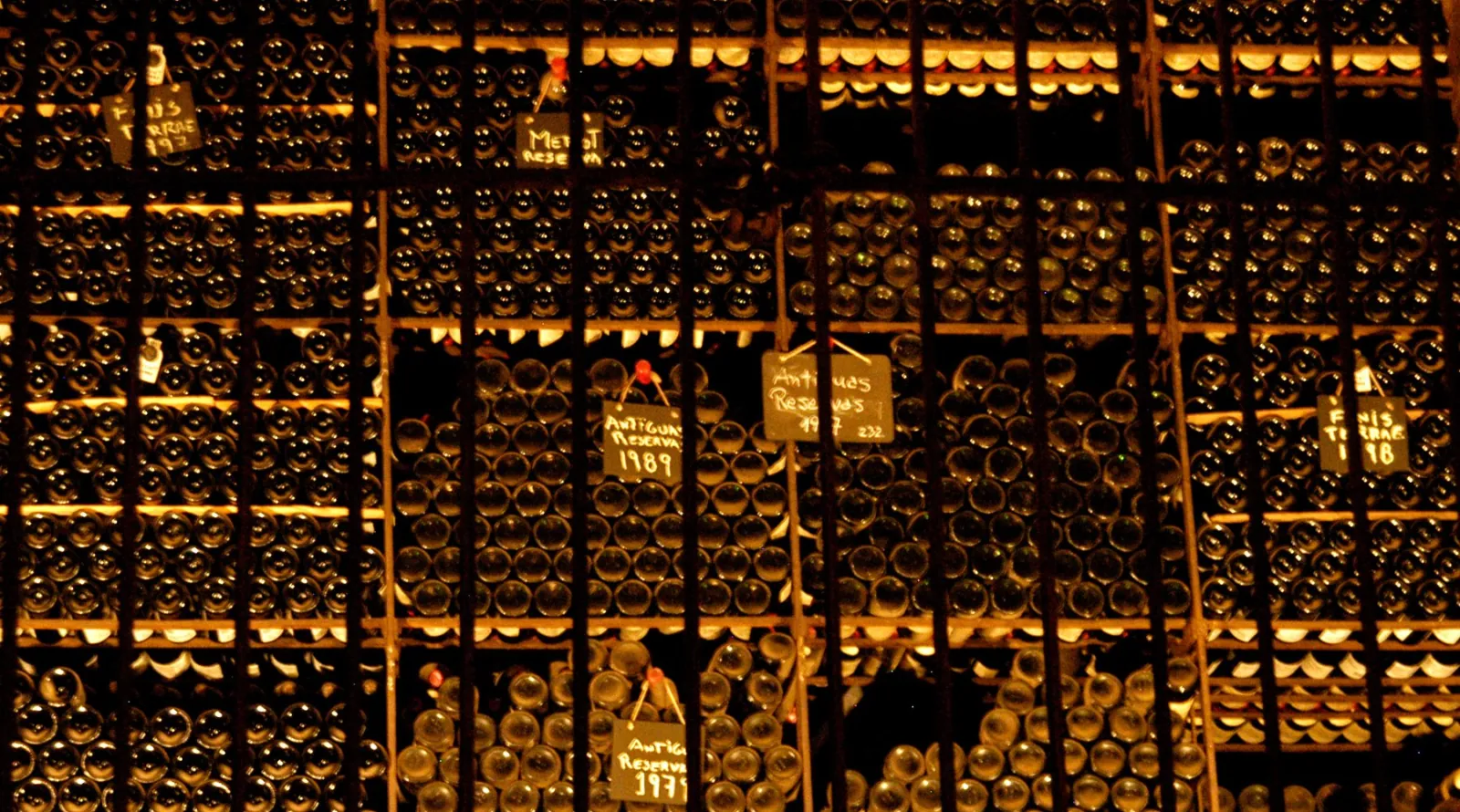 Old wine bottles stacked behind iron bars with handwritten vintage chalkboard labels
