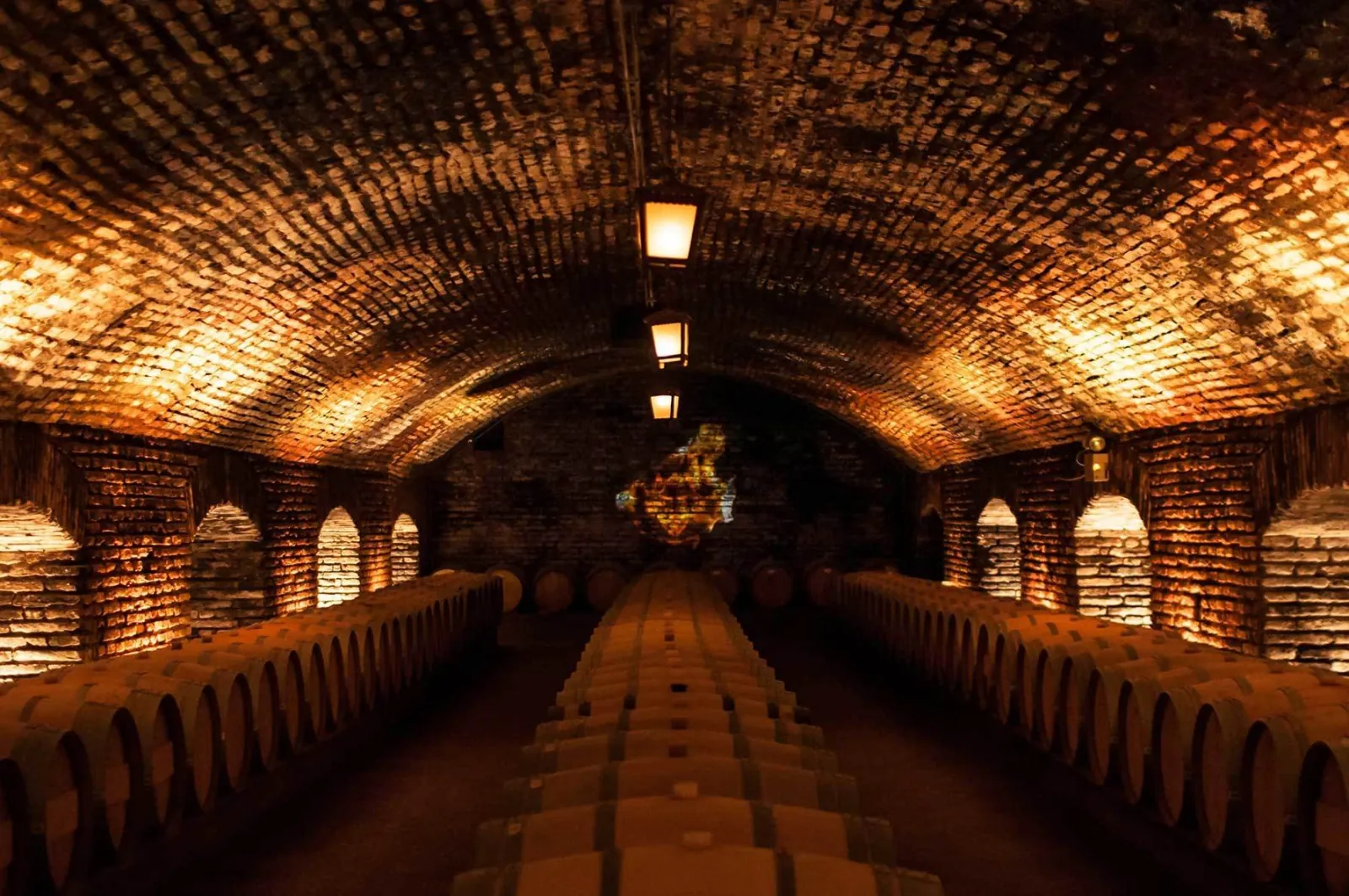 Long vaulted brick cellar with lanterns over rows of oak barrels