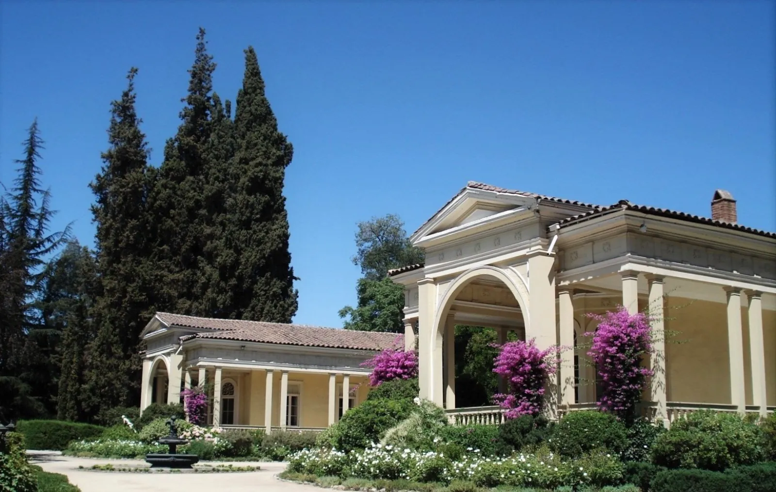 Cream-colored historic house with columns and pink bougainvillea under blue sky