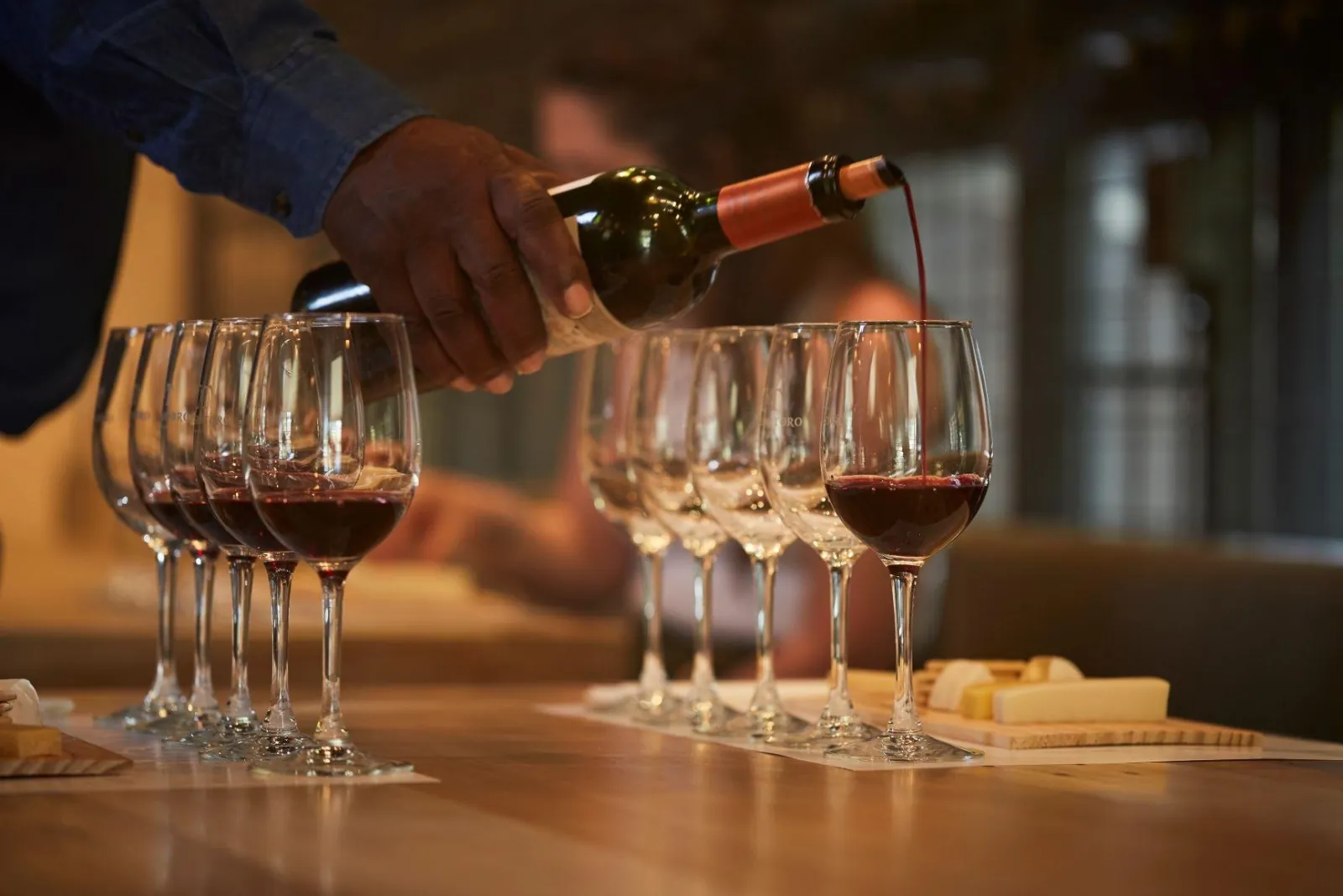 Red wine poured into a row of tasting glasses beside a cheese board