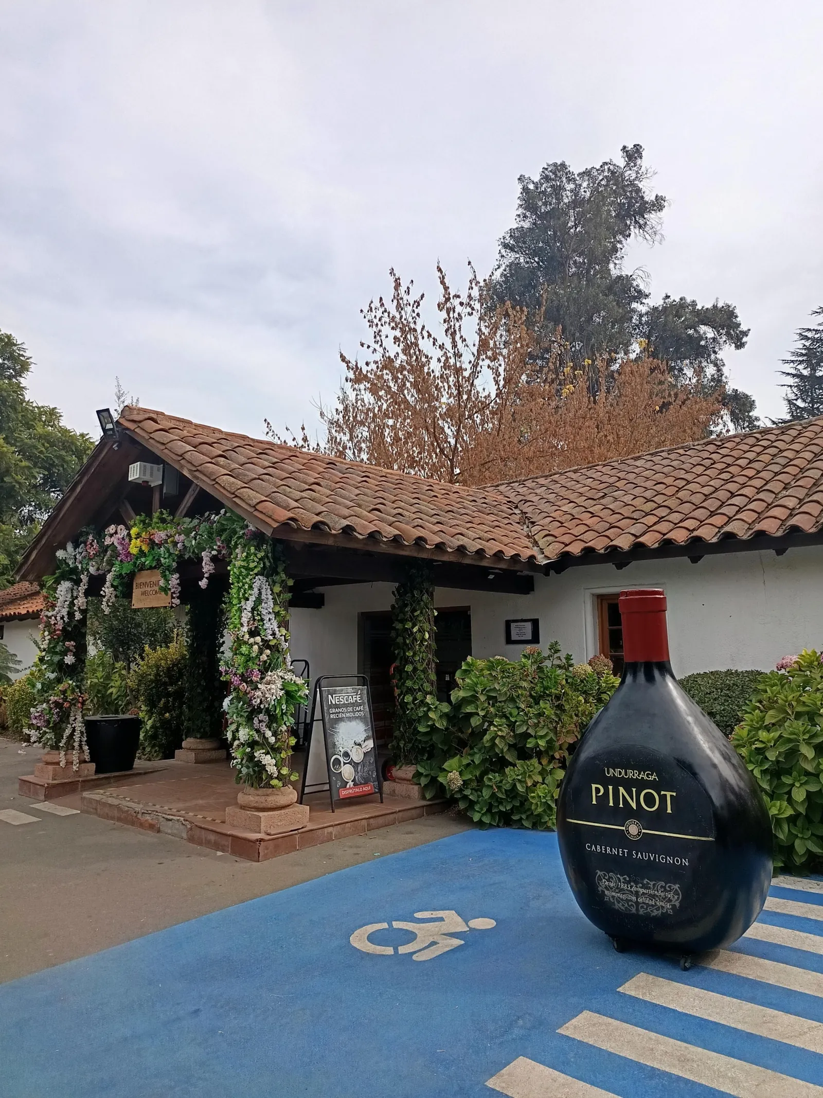 Flower-covered entrance to a tiled-roof building with a giant Undurraga bottle