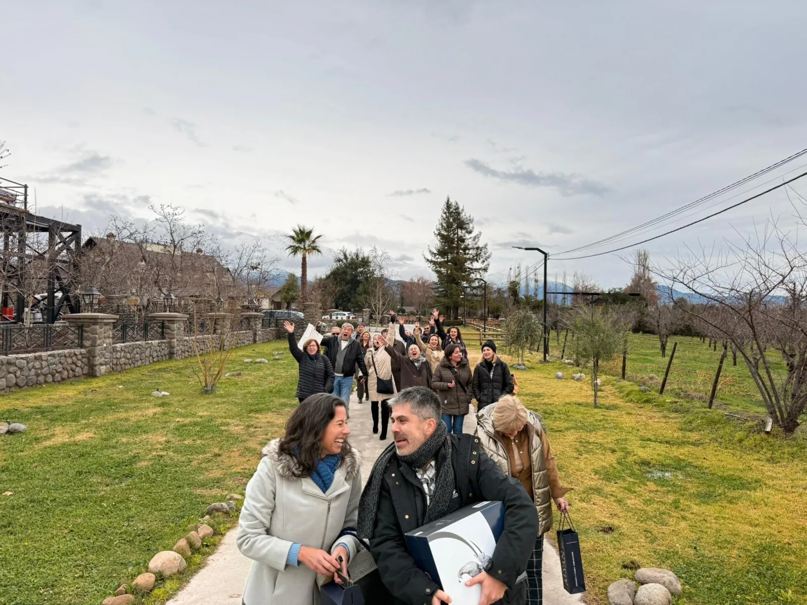 Group of visitors in winter coats walking along a garden path and waving