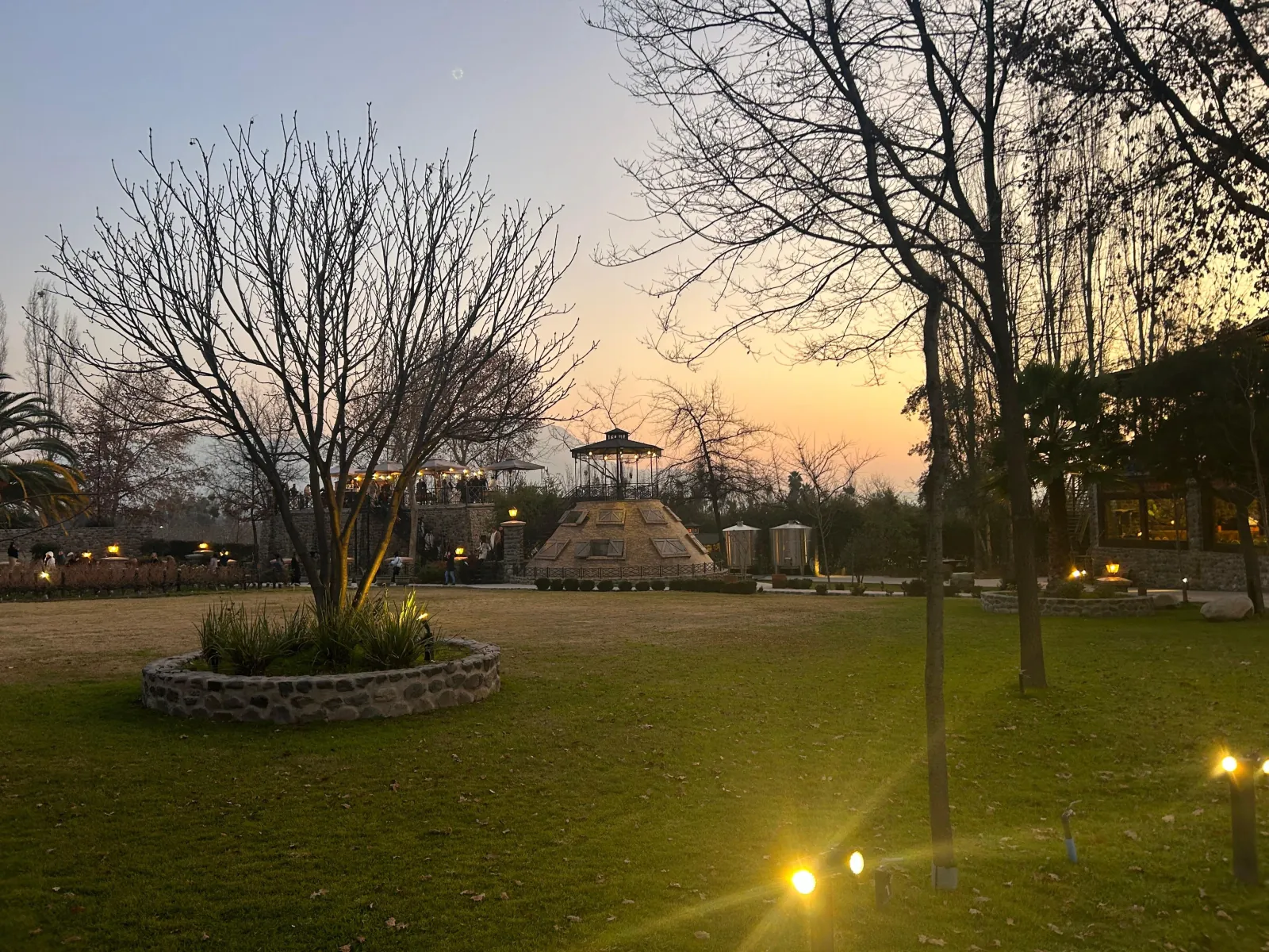 Winery lawn and lit gazebo tower under an orange sky at dusk