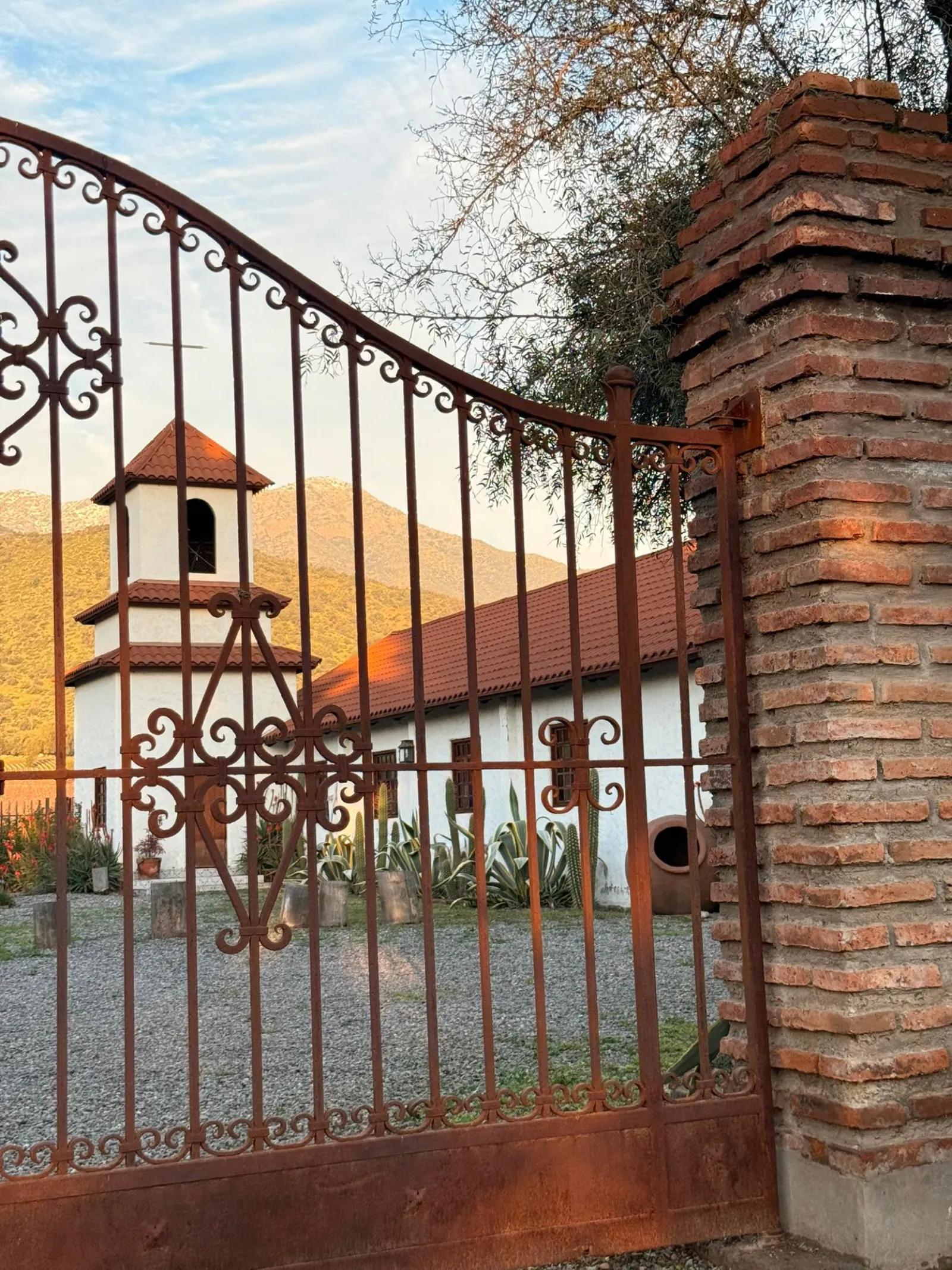 Iron gate framing a white chapel with a bell tower and mountains behind