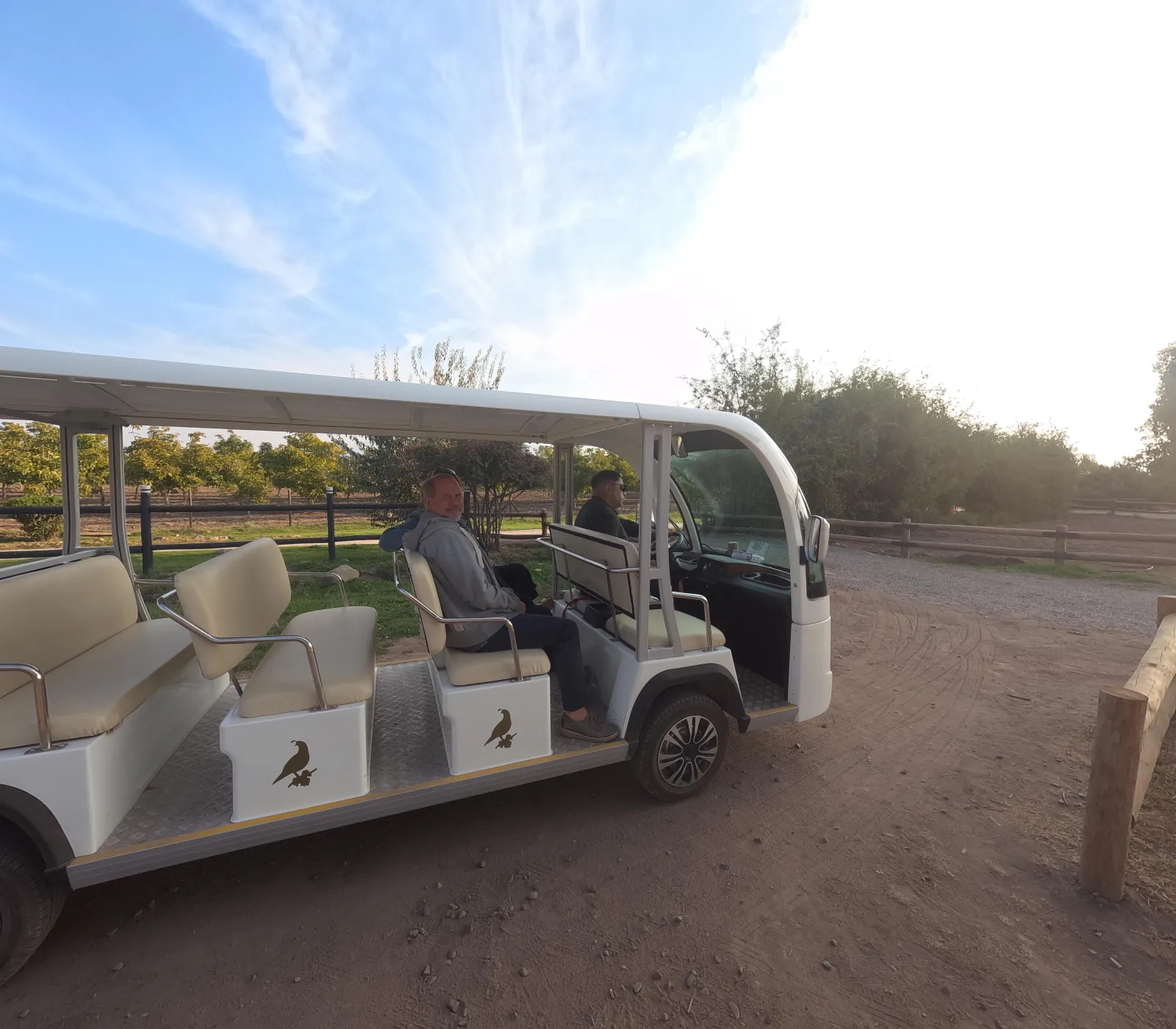 Open electric shuttle cart with passengers parked on a dirt estate road