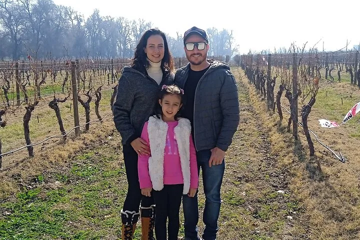 Family of three standing among bare winter vines on a sunny day