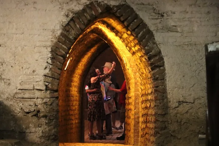 Visitors framed by a lit brick archway inside an old wine cellar