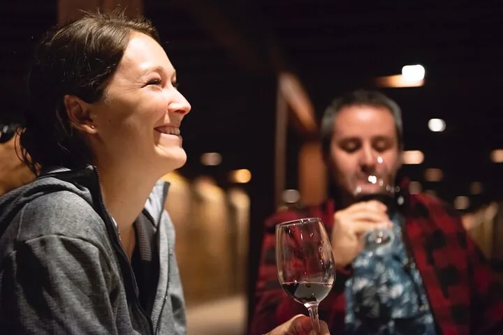 Woman laughing with a glass of red wine in a dim barrel room