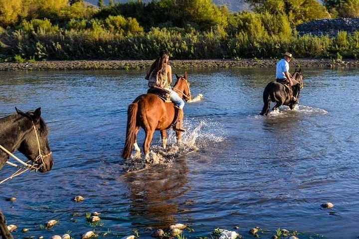 Two riders crossing a shallow river on horseback in evening light