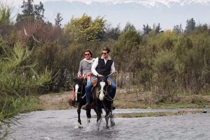 Two riders splashing through a stream with snowy Andes behind