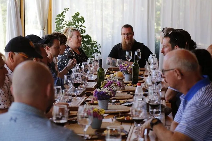 Guests at a long lunch table with wine glasses and small flower vases