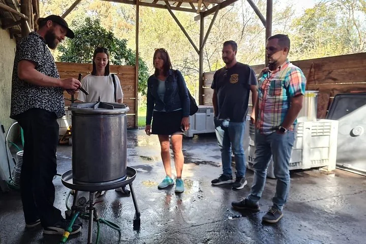 Winemaker explaining a steel press to visitors in an open-sided work shed