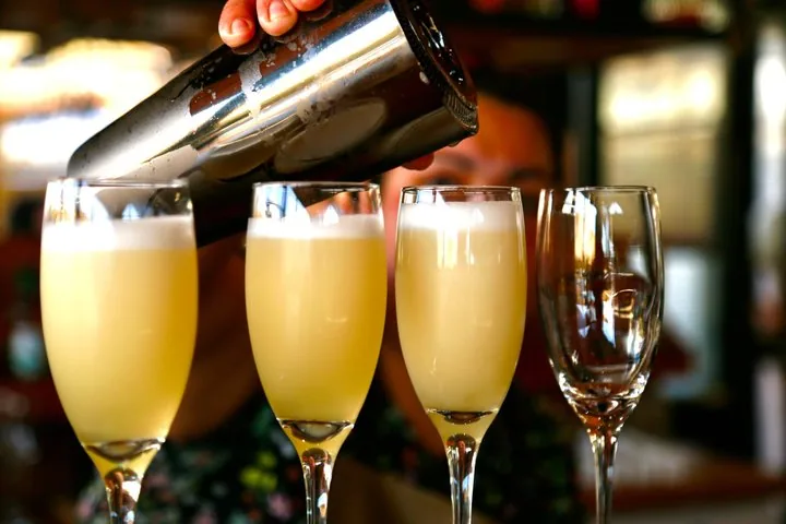 Bartender pouring frothy pisco sours into three tall glasses