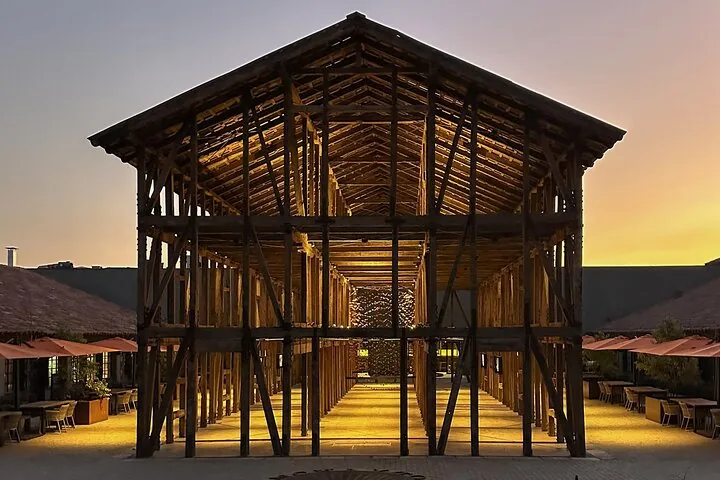 Open timber-frame pavilion lit at dusk between outdoor dining terraces