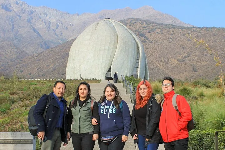Group of visitors posing below the white Bahá'í temple and mountains