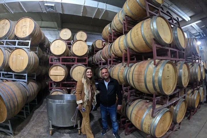 Two visitors standing between stacked oak barrels in a winery cellar